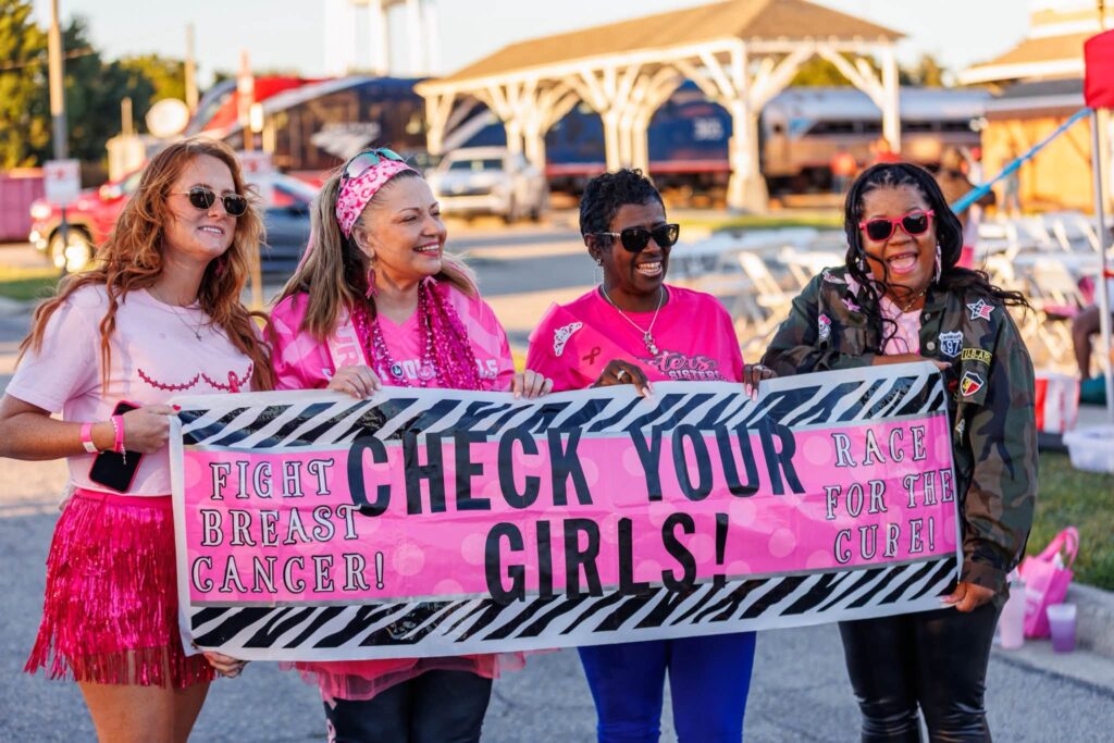 Survivors and supporters holding a pink “Check Your Girls!” banner